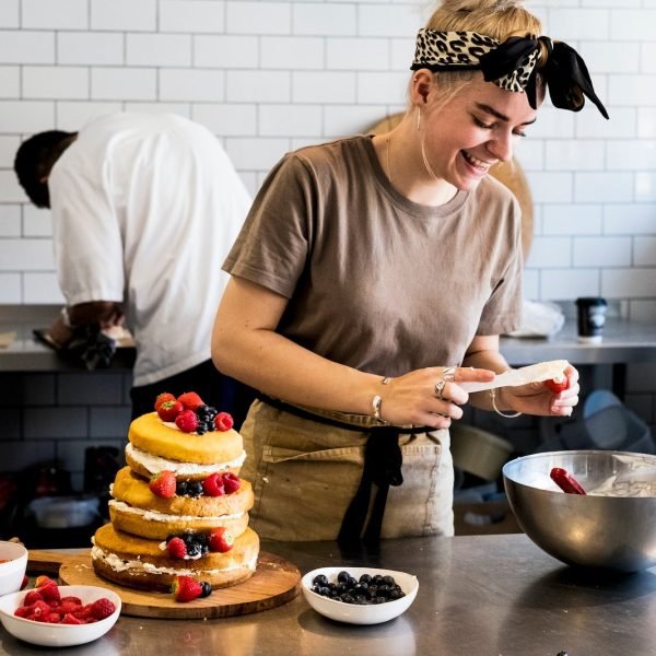 a-cook-working-in-a-commercial-kitchen-assembling-a-layered-sponge-cake-with-fresh-fruit-.jpg